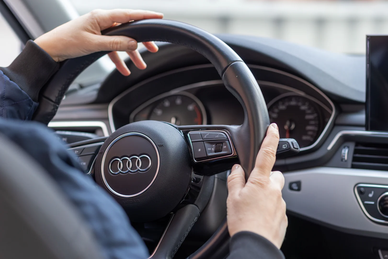 Two hands holding the steering wheel in a view of a car's dashboard